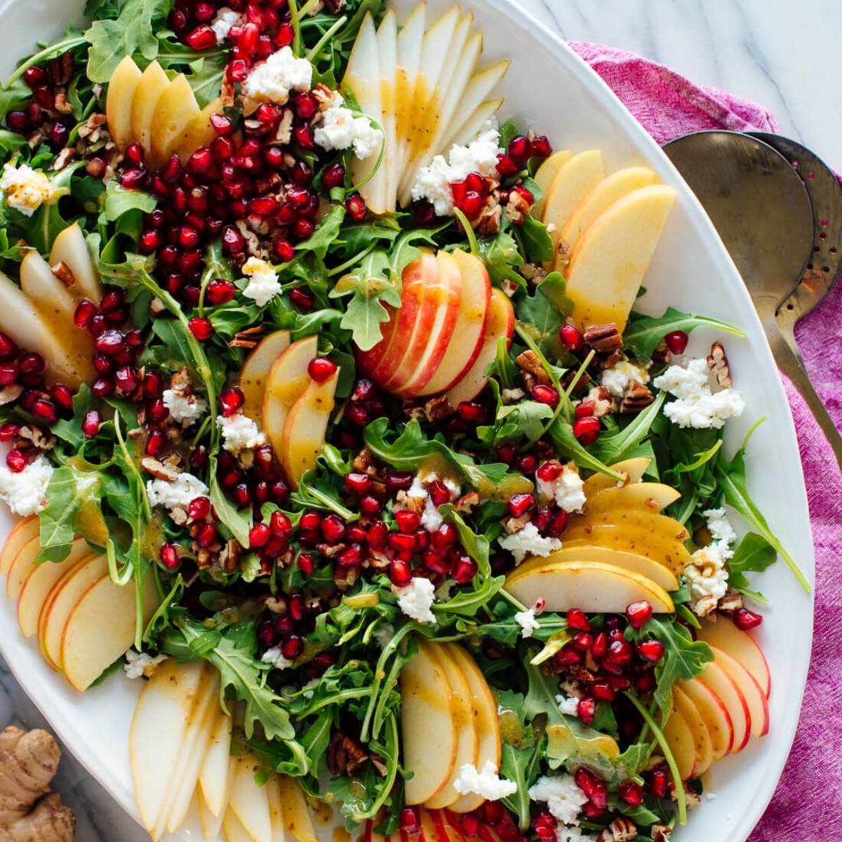 A vibrant salad with arugula, pears, apples, pomegranate seeds, feta cheese, and pecans.