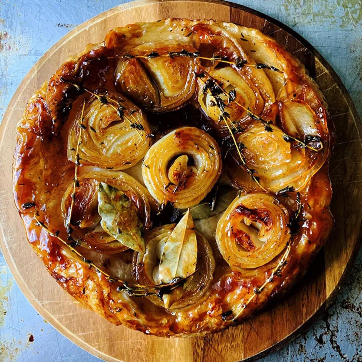 A golden-brown onion tart with caramelized onions and fresh thyme on a wooden board.