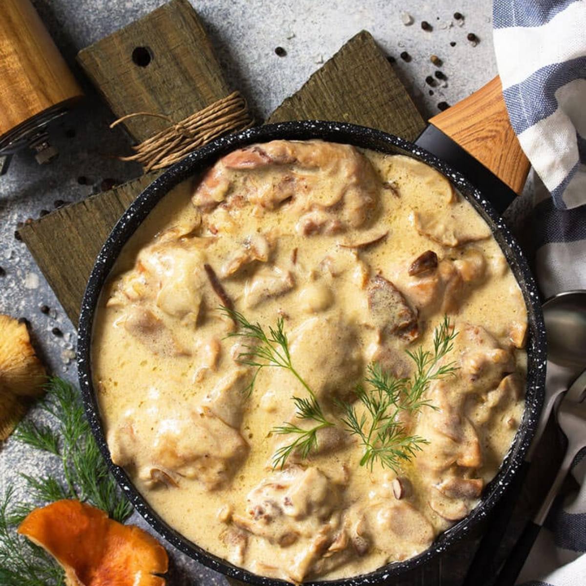 A skillet filled with a creamy mushroom pheasant dish. The meat is tender and covered in a rich, creamy sauce with mushrooms. A sprig of dill adds a touch of freshness.