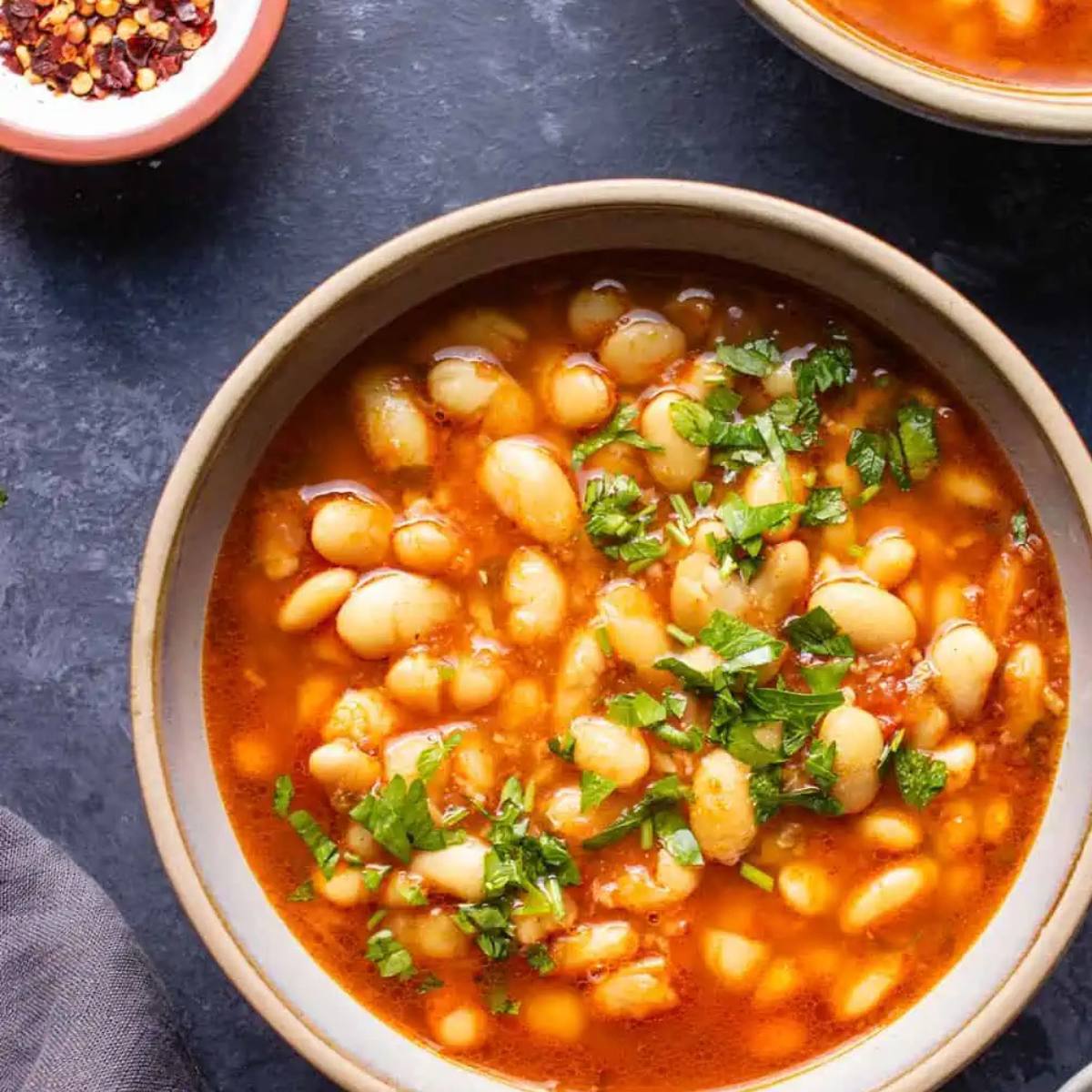 A bowl of hearty white bean soup with a tomato broth. The soup is topped with fresh parsley.







