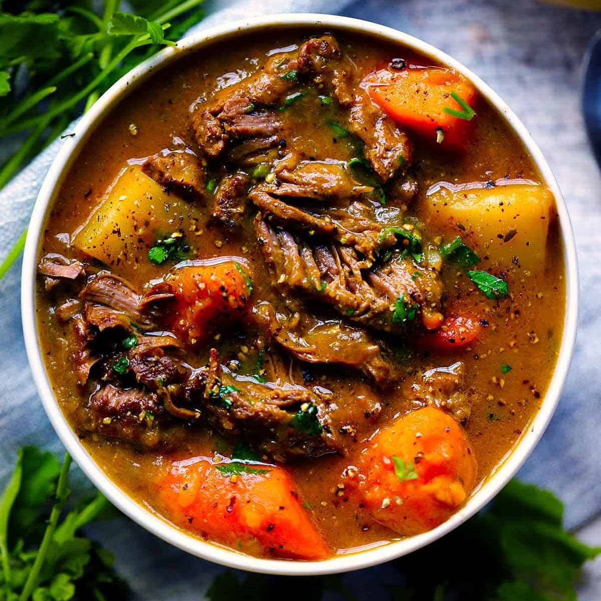 A white bowl filled with a hearty beef stew. The stew is made with tender chunks of beef, carrots, potatoes, and a rich, flavorful gravy.