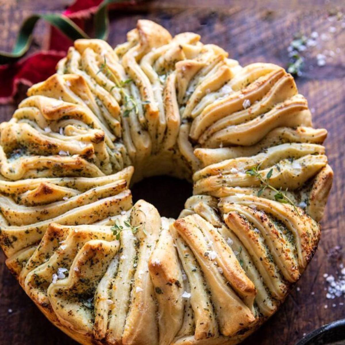 A golden-brown pull-apart bread wreath with herbs and sea salt.