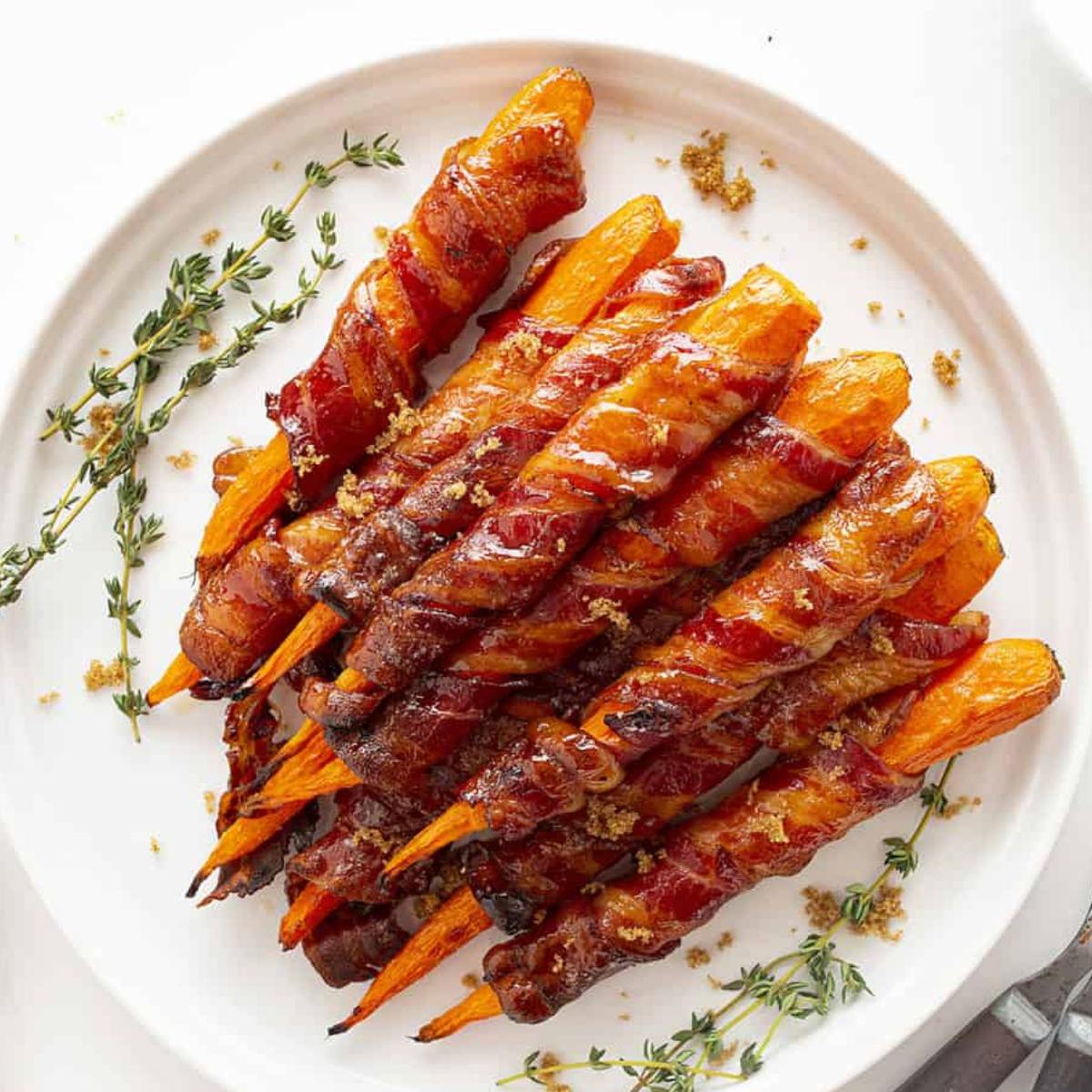 A plate of bacon-wrapped carrots, sprinkled with brown sugar and fresh thyme.