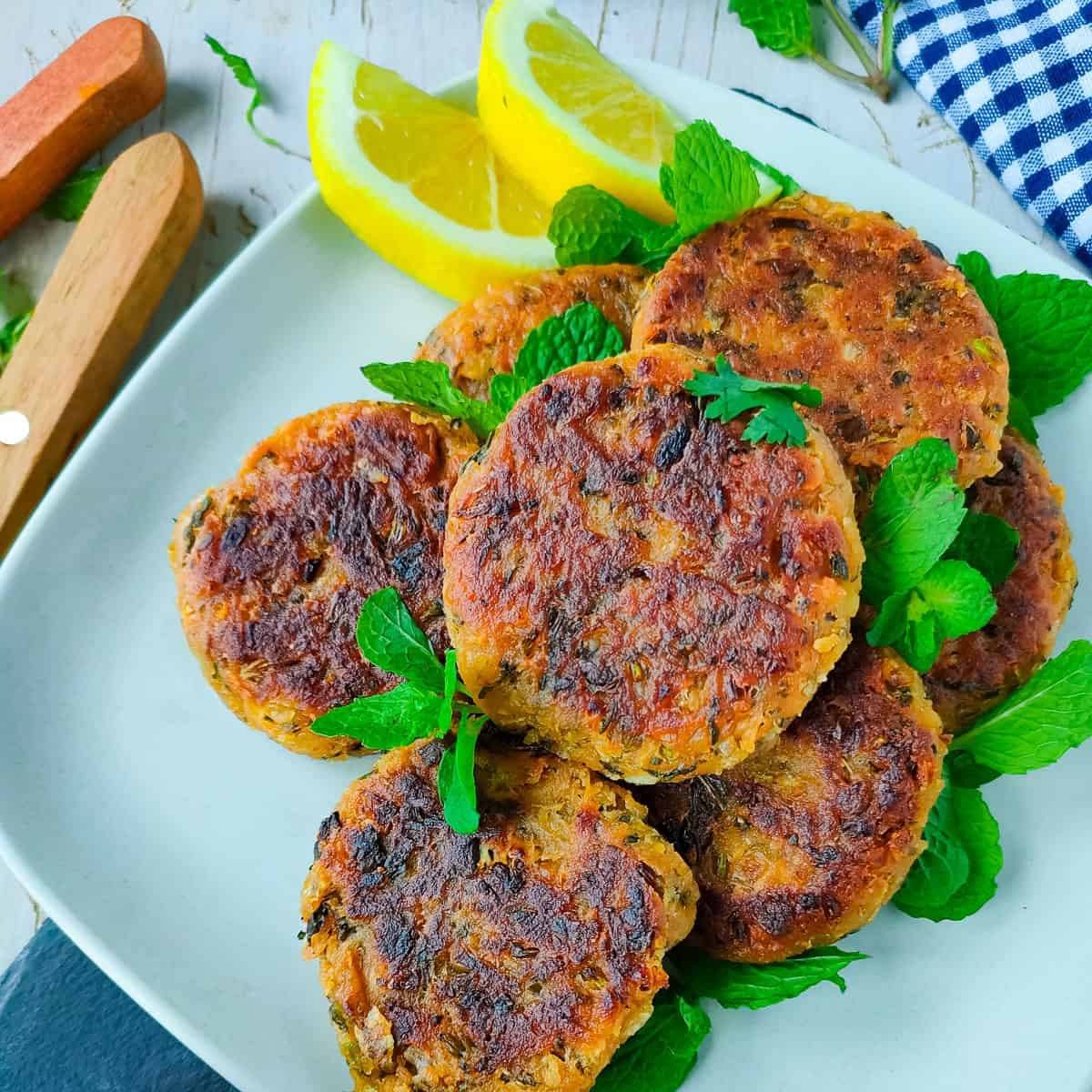 A plate of crispy, golden-brown fritters with fresh mint leaves and lemon wedges.