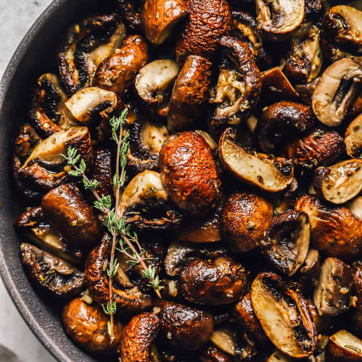 A close-up of sautéed mushrooms in a skillet with fresh thyme.