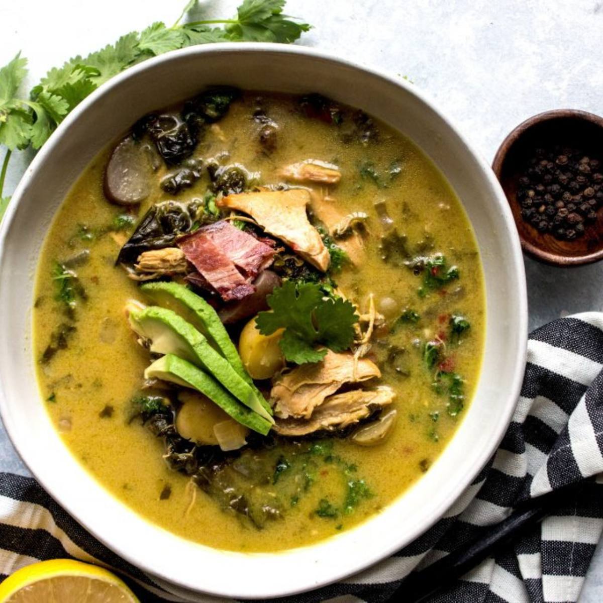 A bowl of hearty chicken and kale soup with avocado, bacon, and potatoes. 