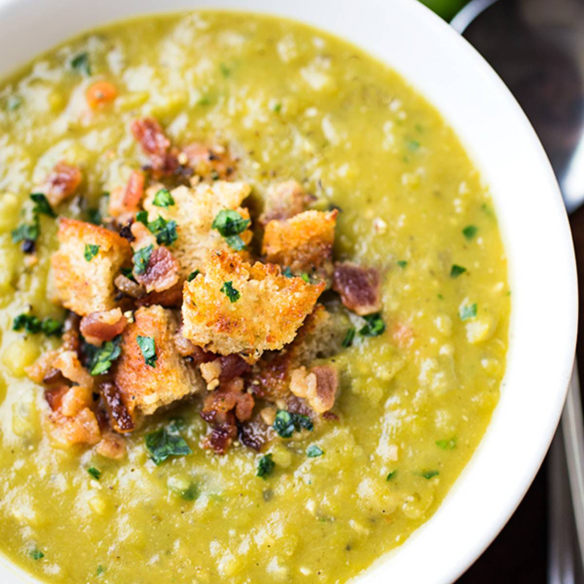 A bowl of creamy split pea soup topped with crispy bacon and croutons.