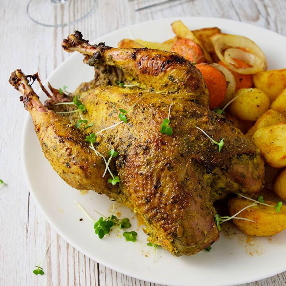 A roasted pheasant with crispy skin, served on a plate with roasted root vegetables. The pheasant appears to be seasoned with herbs and spices.