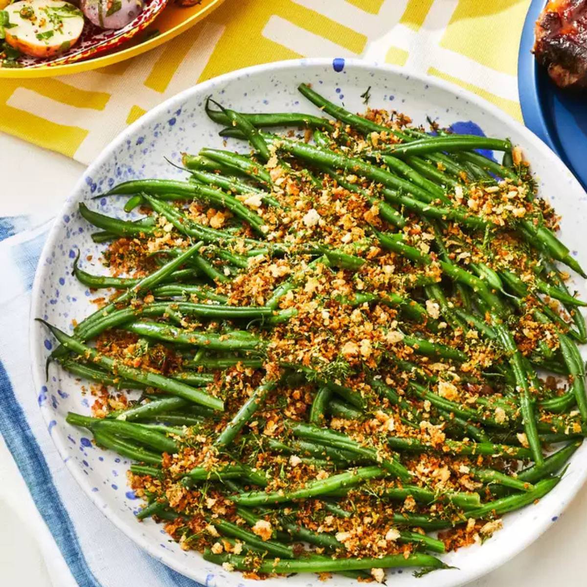 A plate of green beans topped with a herb and breadcrumb mixture.