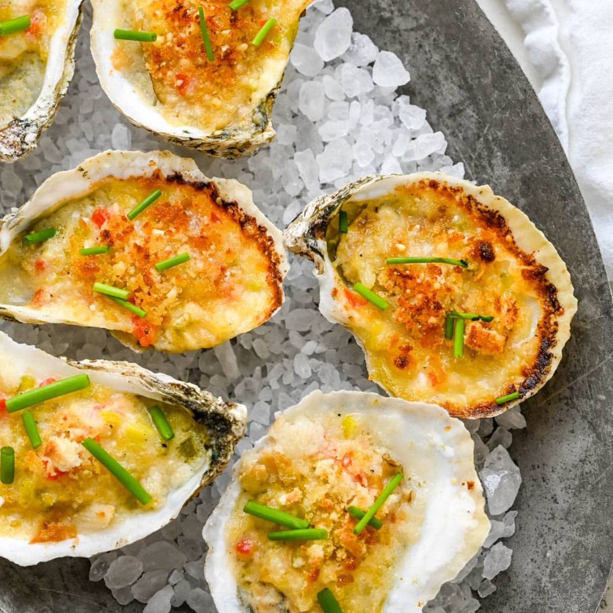 A platter of baked oysters topped with a creamy, cheesy filling and garnished with chopped chives.