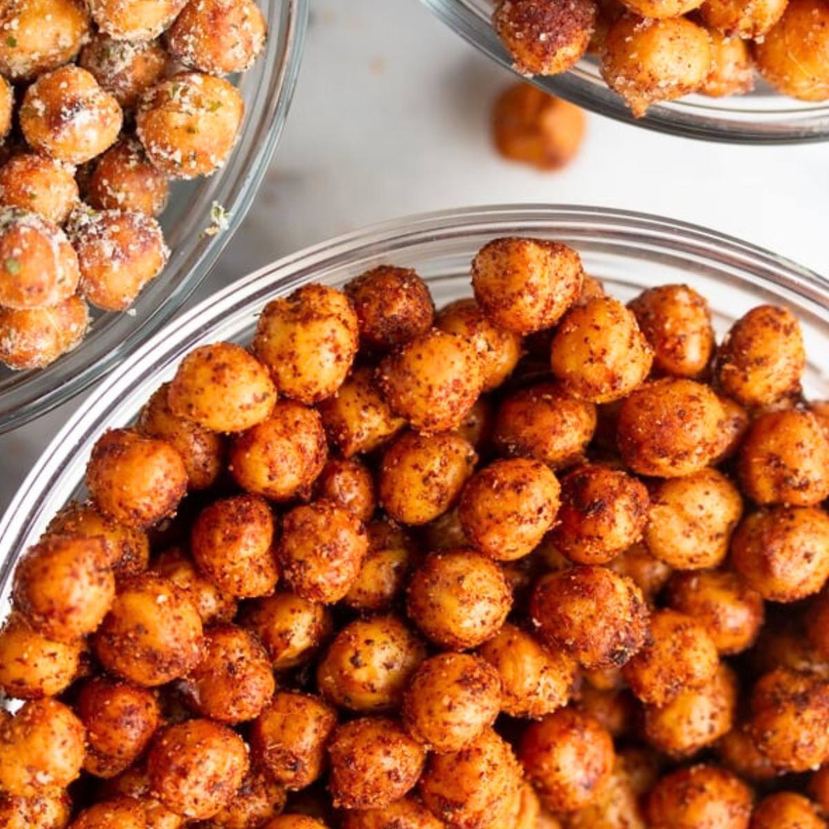 A close-up of two bowls of roasted chickpeas. One bowl contains chickpeas seasoned with a savory herb blend, and the other bowl contains chickpeas seasoned with a spicy paprika blend.