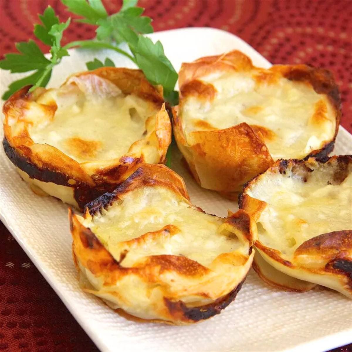 A plate of four golden-brown baked brie cups with a sprig of parsley.