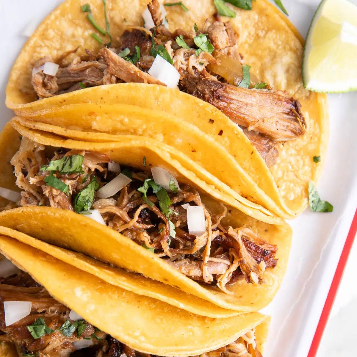 A plate of four crispy tacos filled with shredded pork, garnished with cilantro and onion.