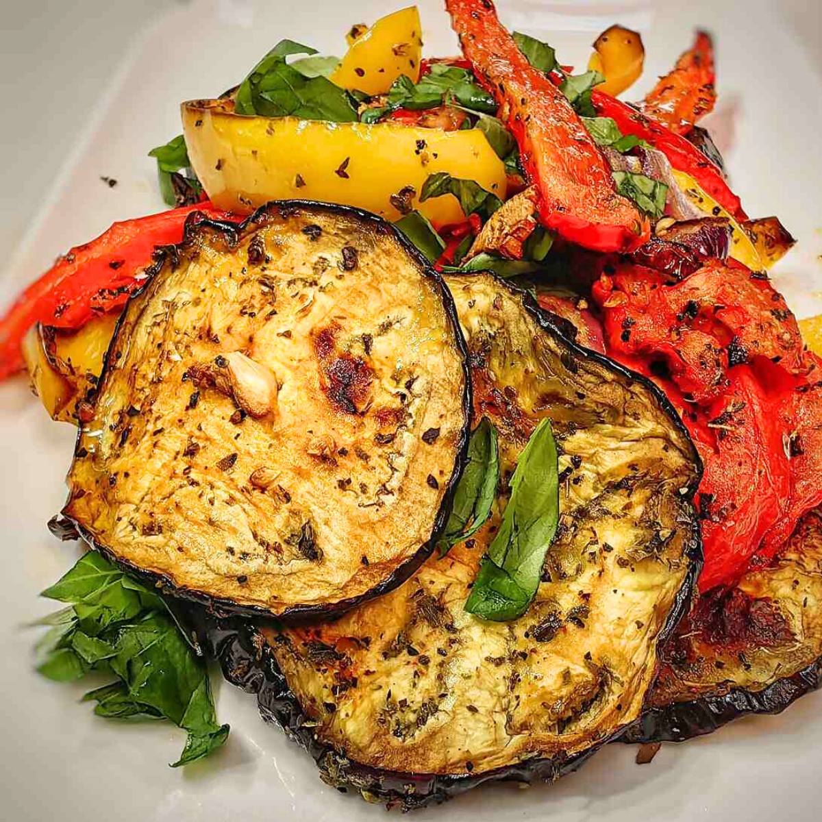 A plate of grilled eggplant, bell peppers, and tomatoes with fresh basil.