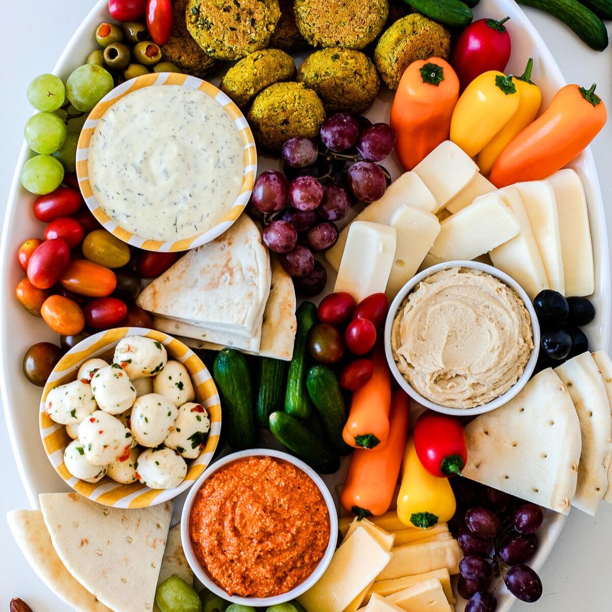 A large platter with a variety of Mediterranean appetizers, including falafel, hummus, pita bread, olives, cheese, grapes, and vegetables.