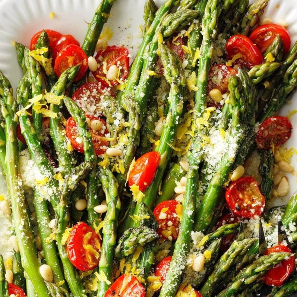 A plate of roasted asparagus with cherry tomatoes, pine nuts, and Parmesan cheese.