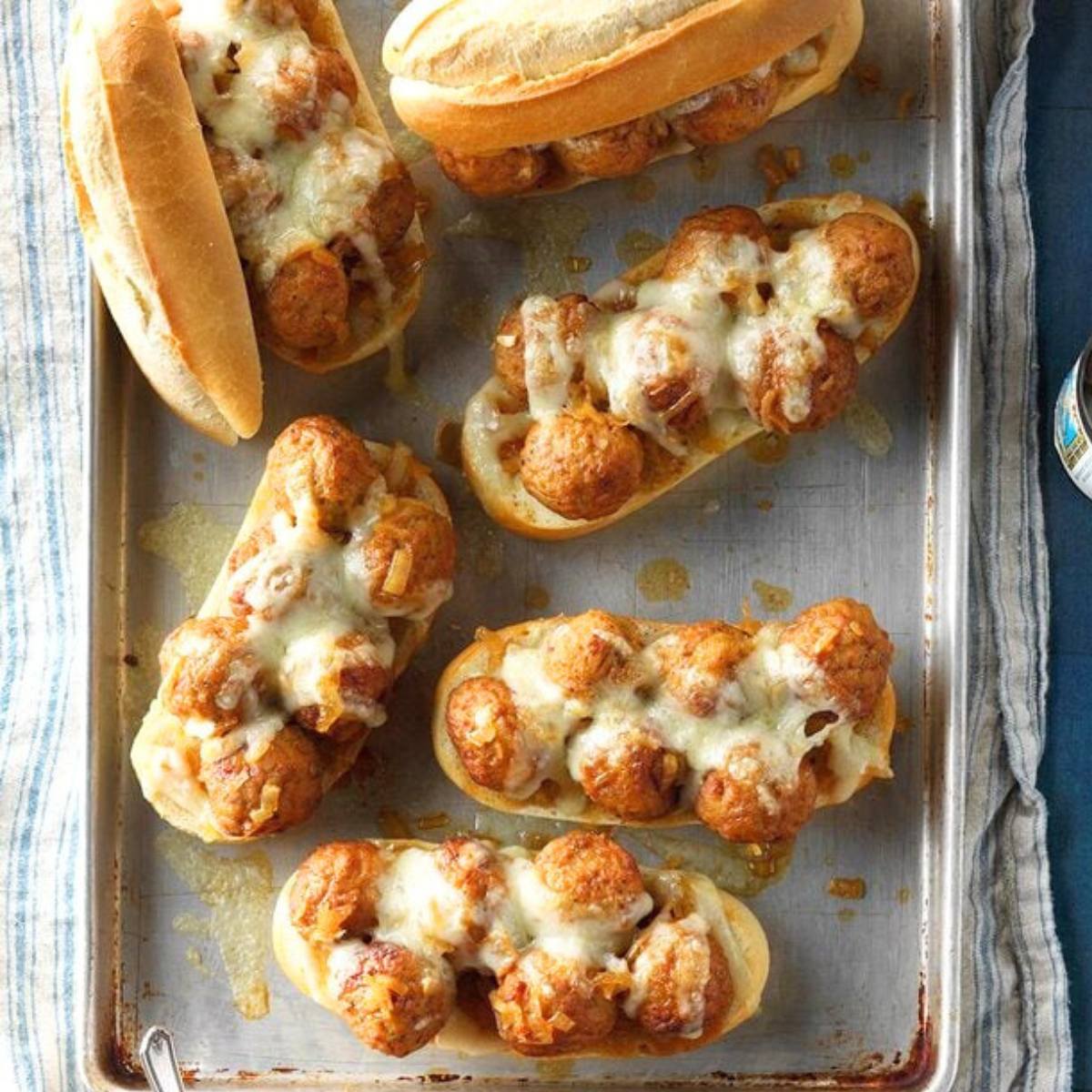 A tray of meatball subs with melted cheese and onions.