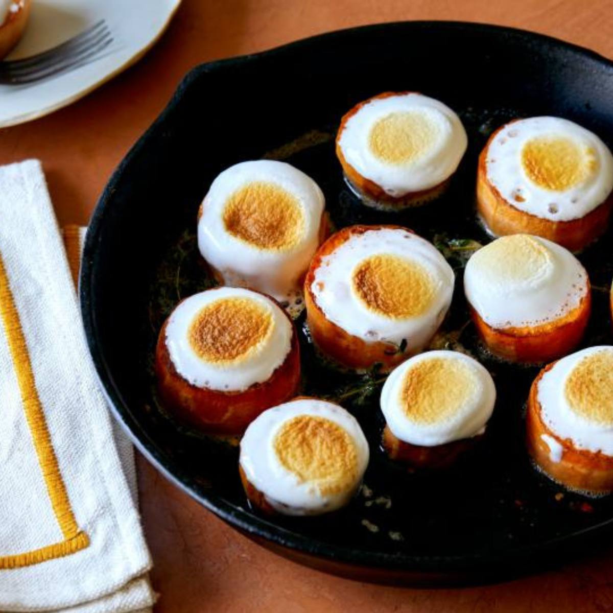 A cast iron skillet with roasted sweet potatoes topped with toasted marshmallows.