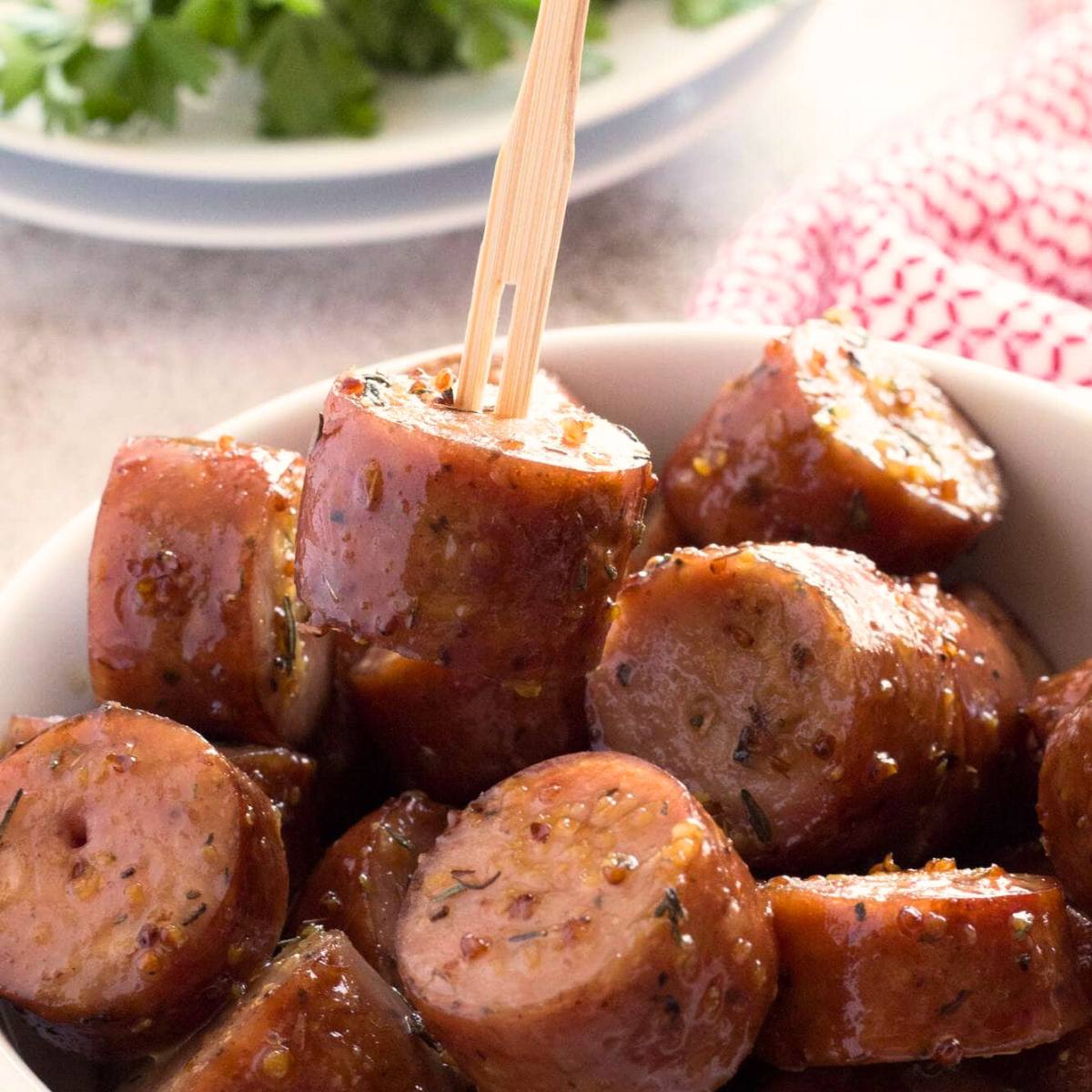 A bowl of glazed, bite-sized sausages with a toothpick sticking out of one.