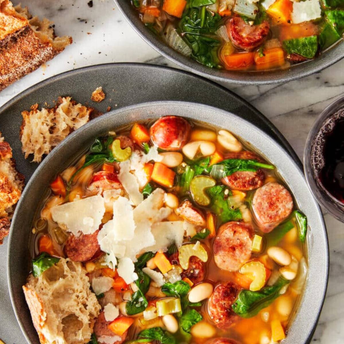 A bowl of hearty sausage and white bean soup with vegetables and Parmesan cheese. 