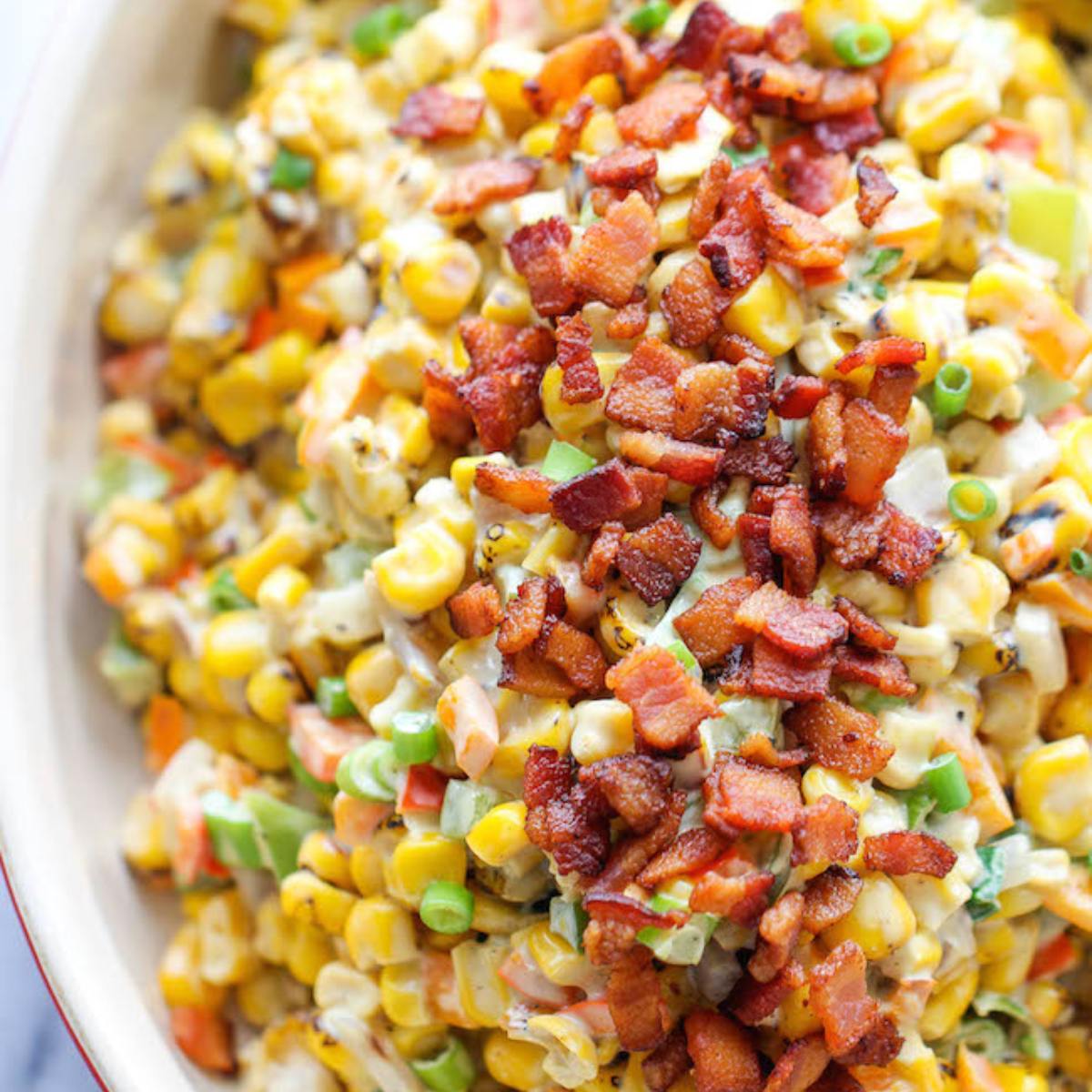 A bowl of creamy corn salad topped with crispy bacon.