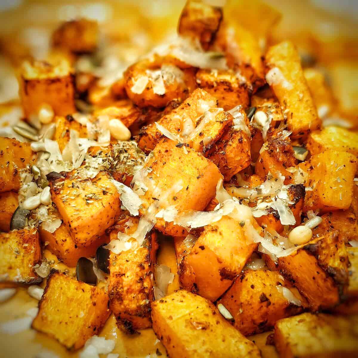 A close-up of roasted butternut squash cubes with pine nuts and Parmesan cheese.