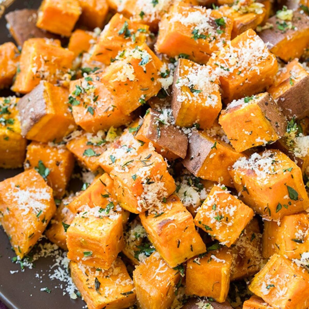 A close-up of roasted sweet potato cubes with herbs and parmesan cheese.