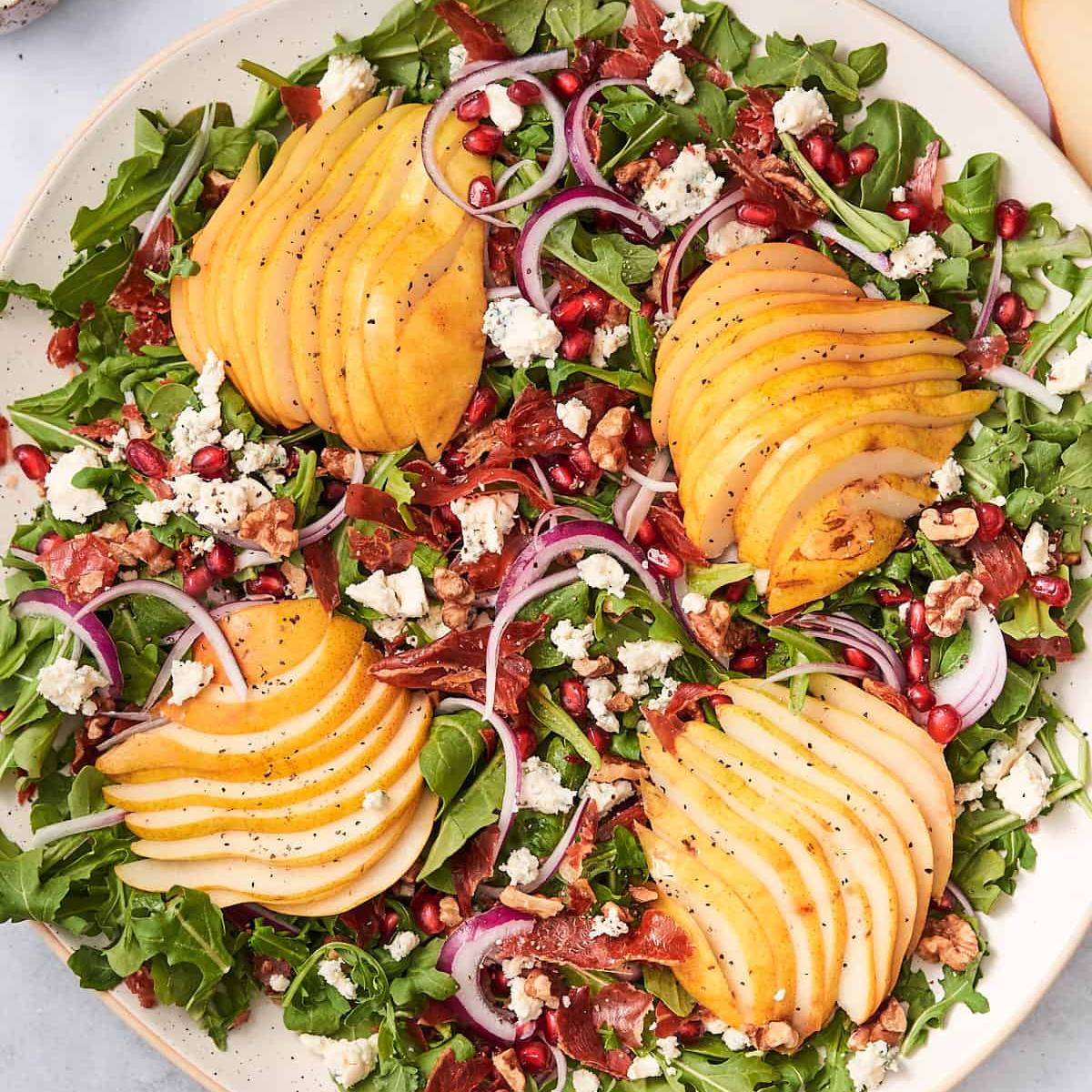 Arugula salad with sliced pears, pomegranate seeds, blue cheese, prosciutto, red onion, and walnuts.