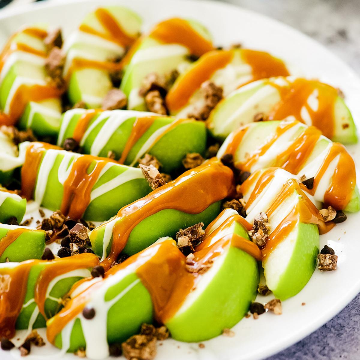 A plate of apple slices drizzled with caramel sauce and white chocolate, topped with chocolate chips.