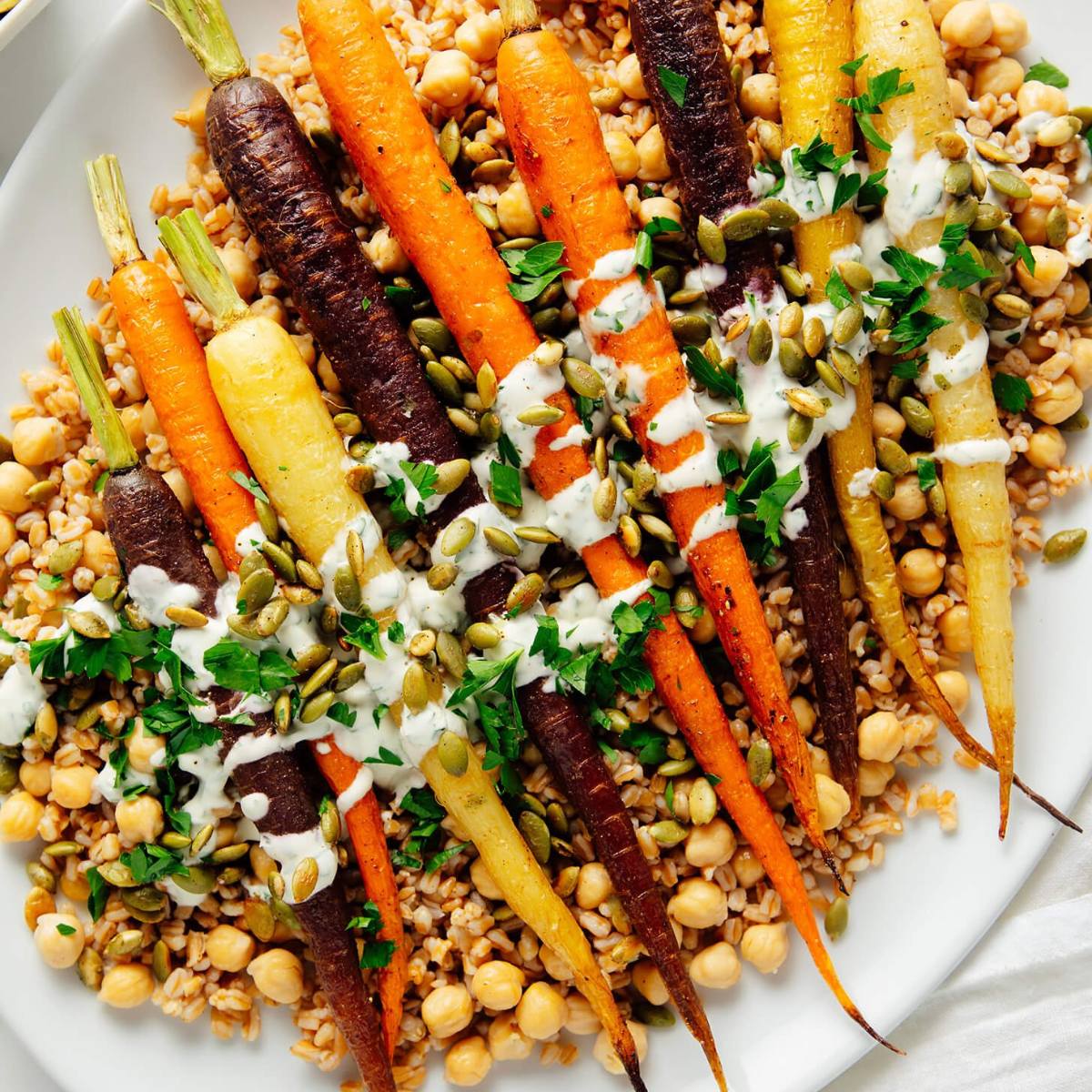 A plate of roasted carrots with chickpeas, farro, and a creamy sauce.