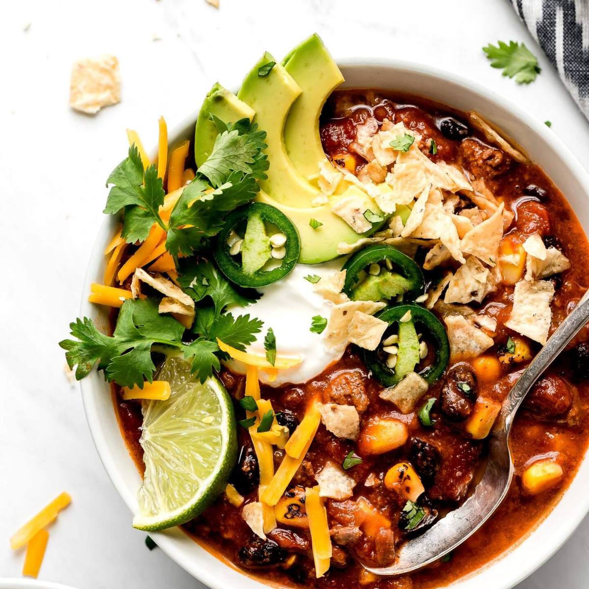 A bowl of hearty taco soup with a variety of toppings. The soup itself is a vibrant red color and filled with beans, corn, and ground beef. 