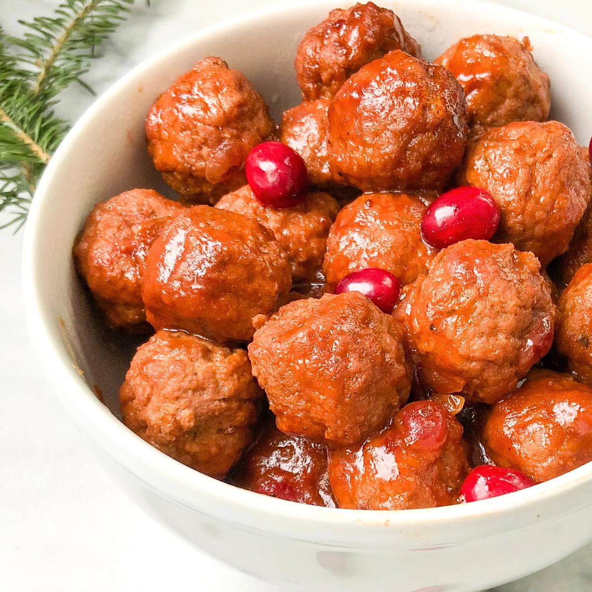 A bowl of meatballs covered in a sweet and tangy sauce with cranberries.