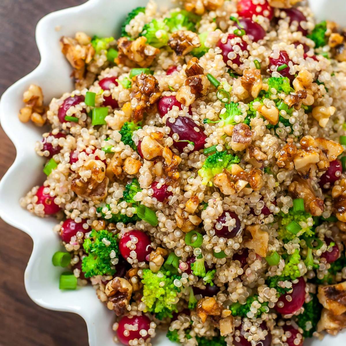 A bowl of quinoa salad with cranberries, broccoli florets, walnuts, and green onions.