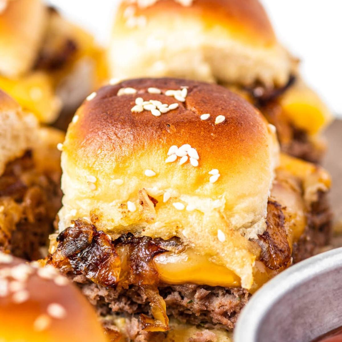 A close-up of a cheeseburger slider with melted cheese, caramelized onions, and sesame seeds on the bun.