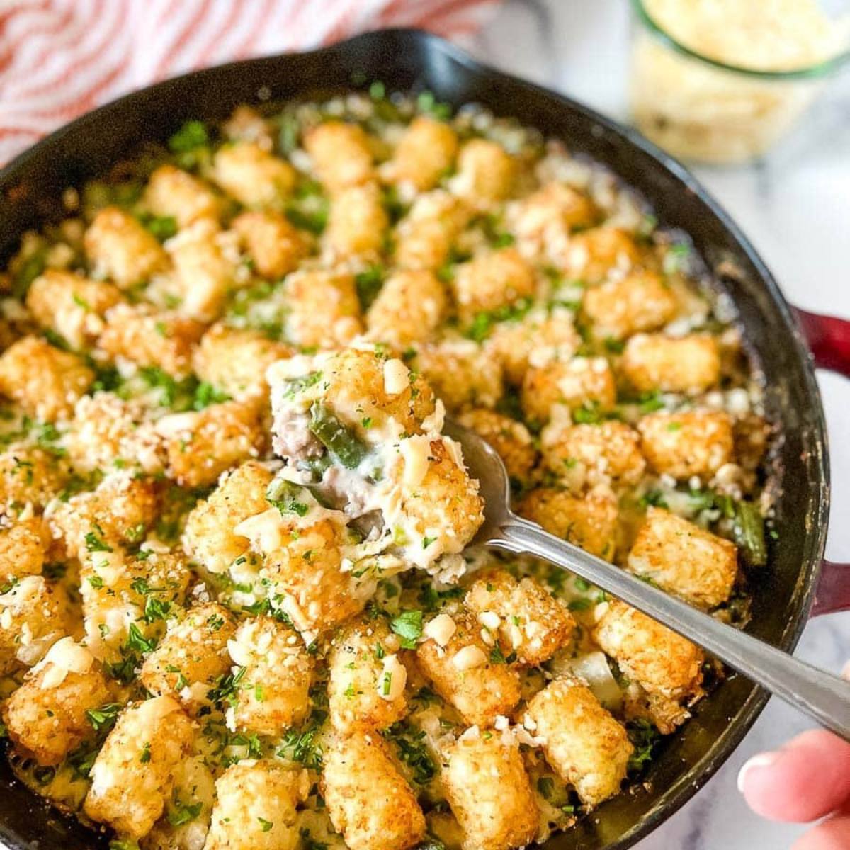 A skillet filled with a cheesy tater tot casserole, with a spoonful being scooped out.