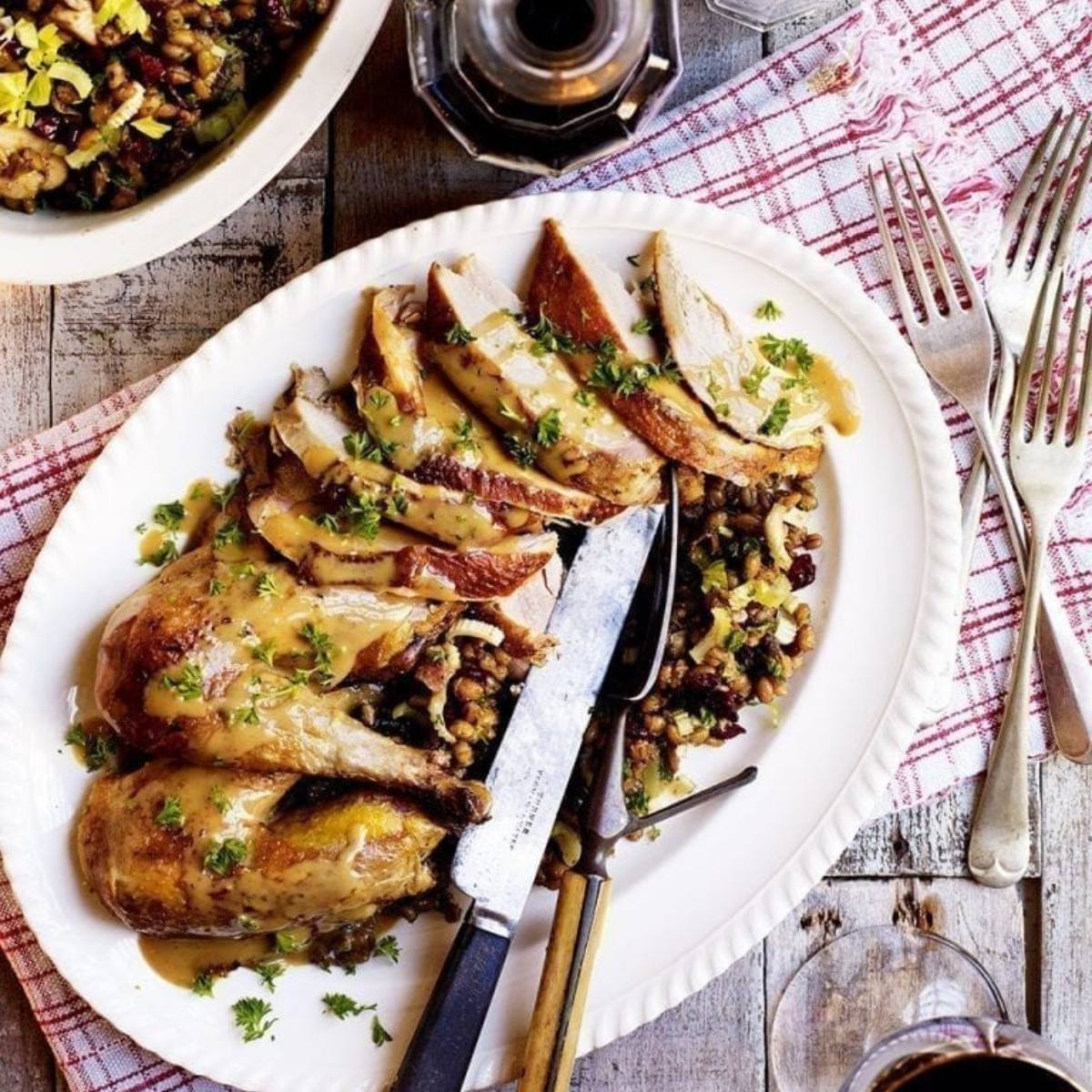 A roasted pheasant sliced and served on a platter with a side dish. The pheasant is golden brown and looks delicious. The side dish appears to be a lentil and cranberry dish.