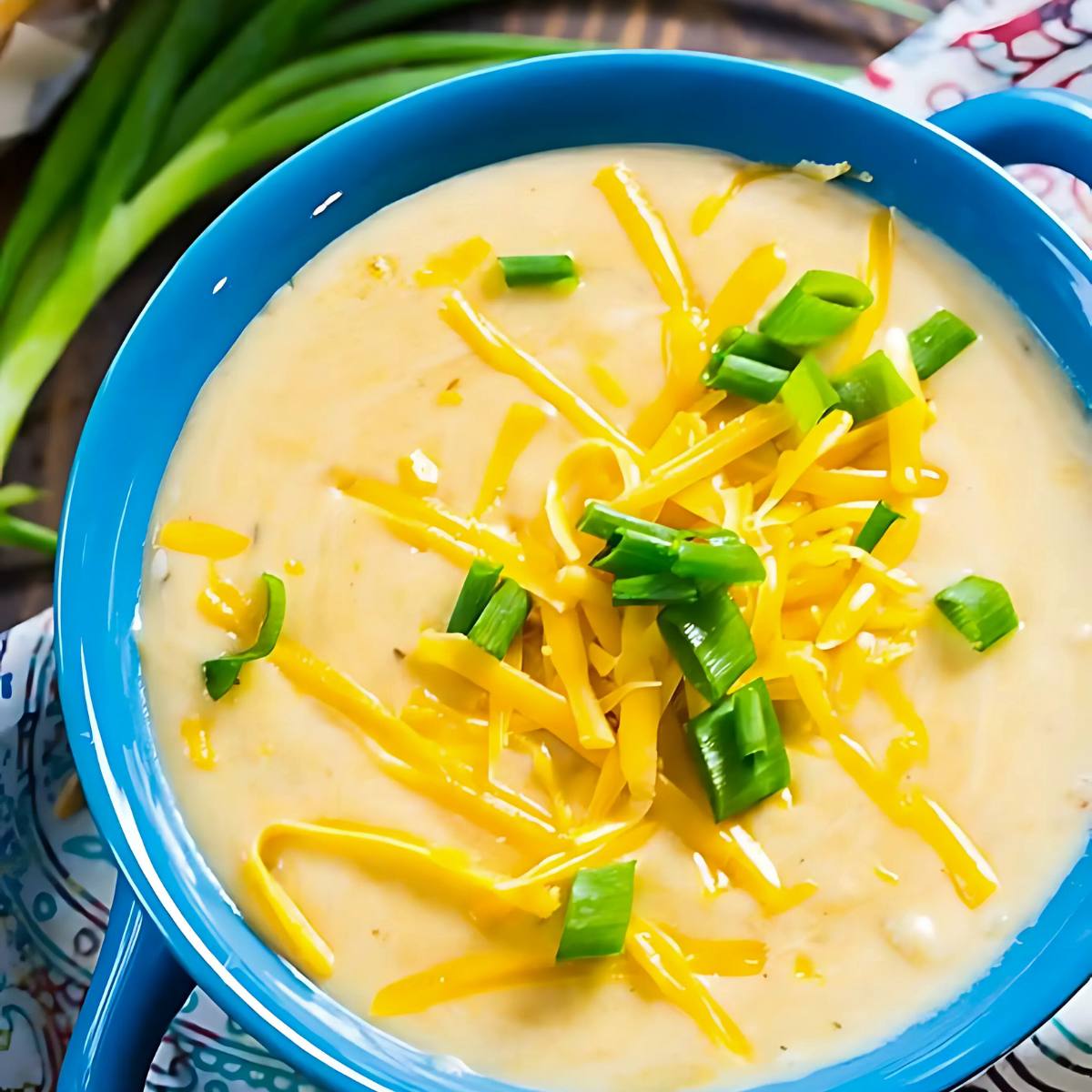 A bowl of creamy, cheesy soup topped with shredded cheese and green onions. 