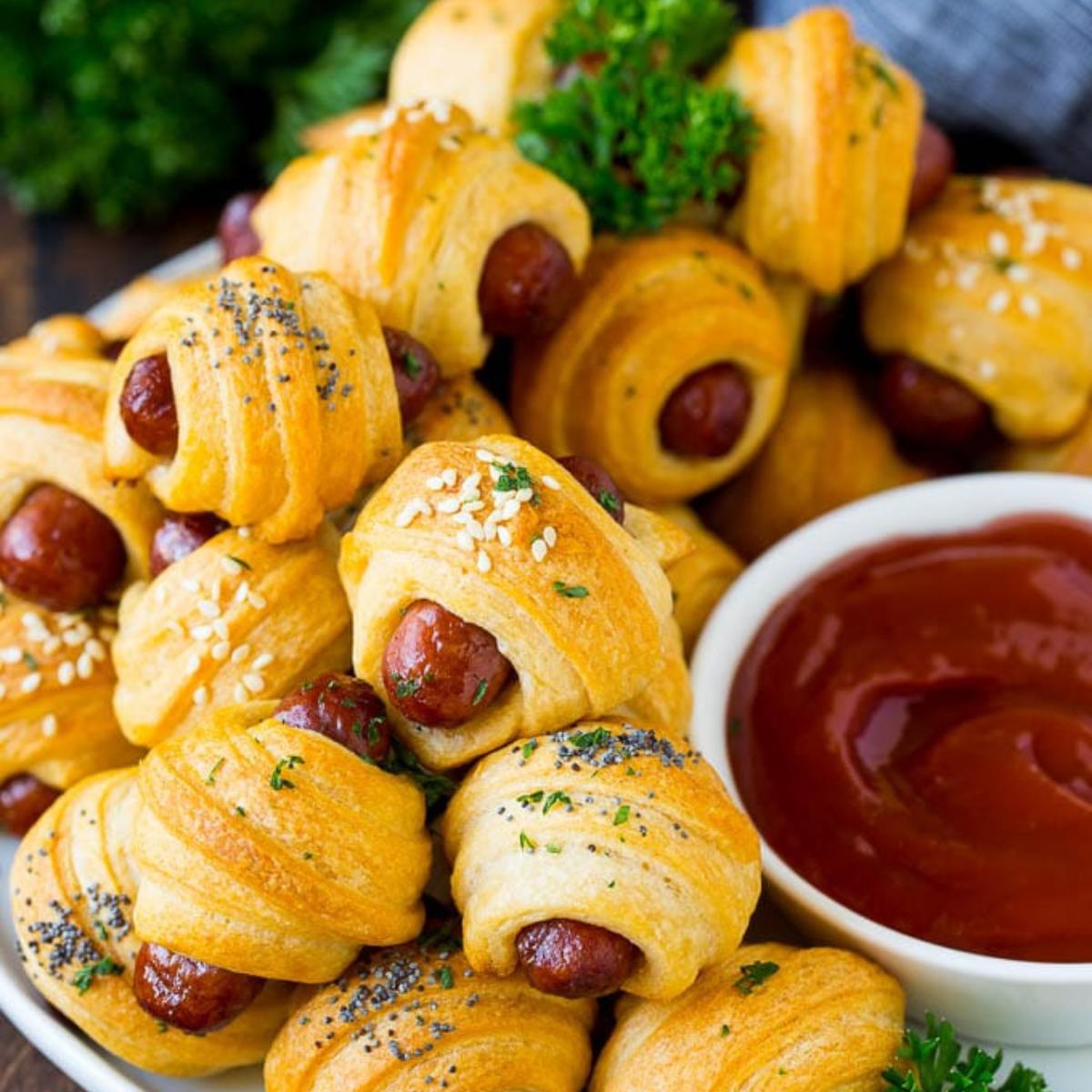 A plate of pigs in a blanket with a side of ketchup.