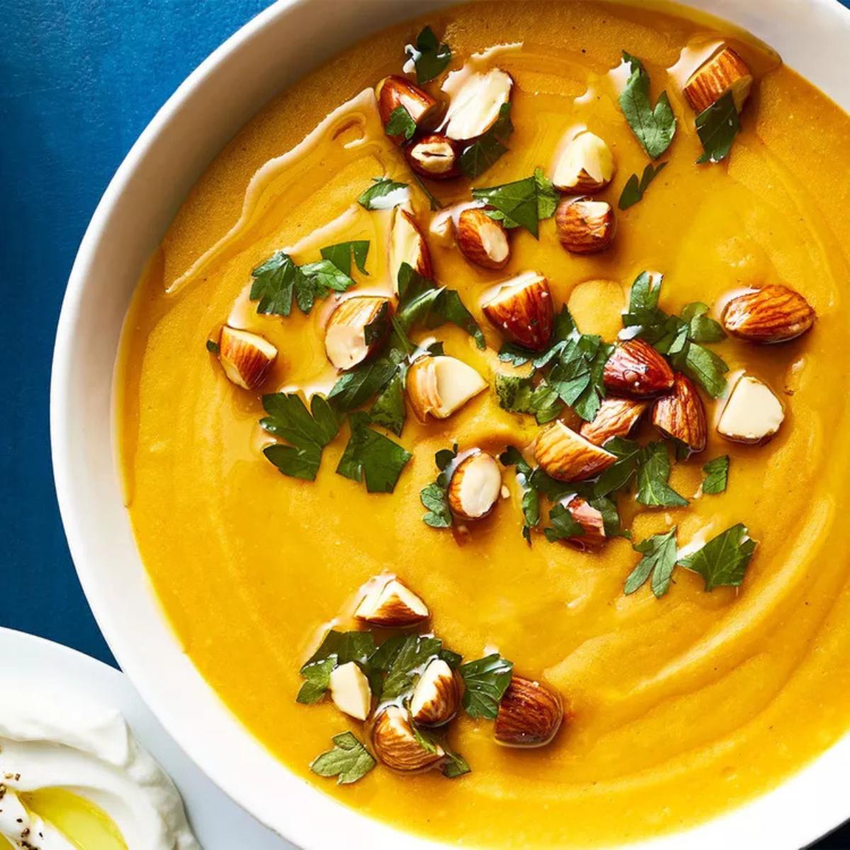 A bowl of creamy, golden soup topped with chopped almonds and fresh parsley.