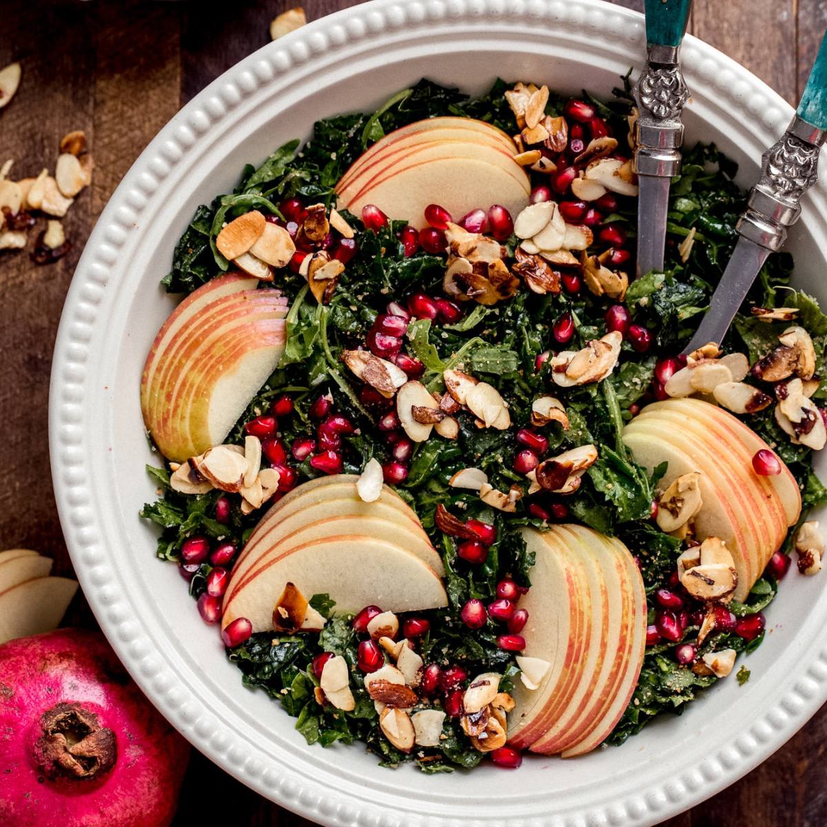 A bowl of kale salad with sliced apples, pomegranate seeds, and toasted almonds.