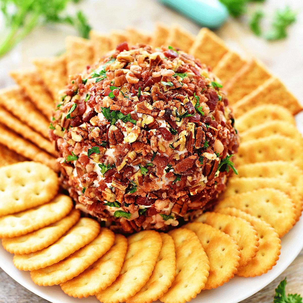 A large, round cheese ball covered in bacon, pecans, and parsley, surrounded by a ring of crackers on a white plate.