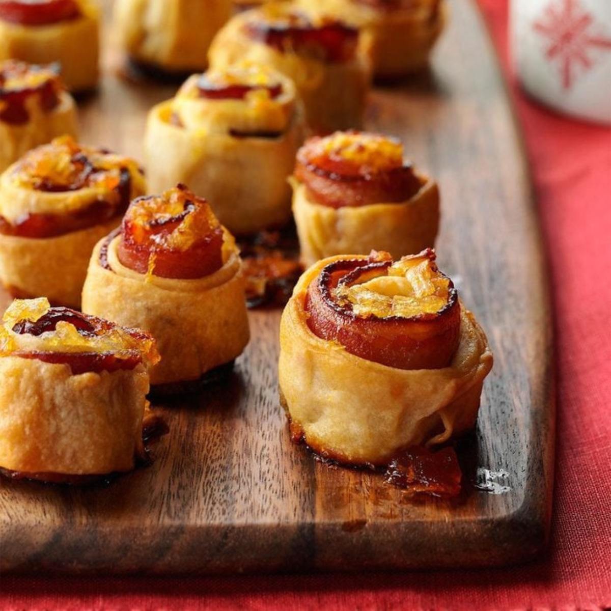 A close-up of several small, golden-brown pastry rolls filled with a sweet and savory filling on a wooden cutting board.