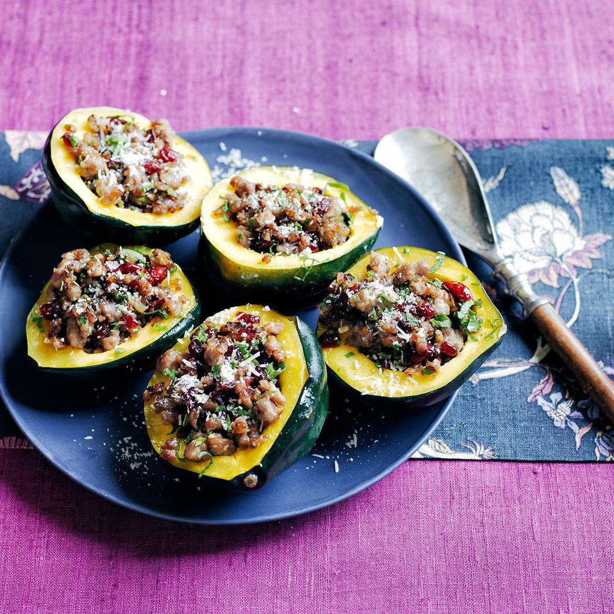 A plate of stuffed acorn squash halves filled with a mixture of sausage, cranberries, and herbs.