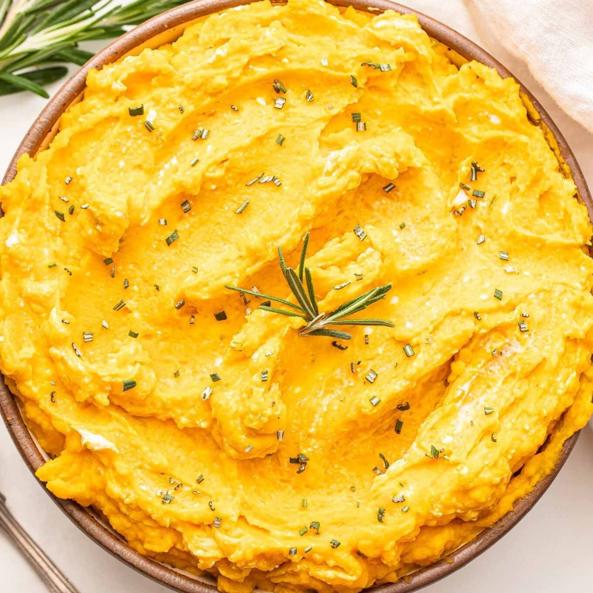 A bowl of creamy mashed sweet potatoes topped with rosemary.