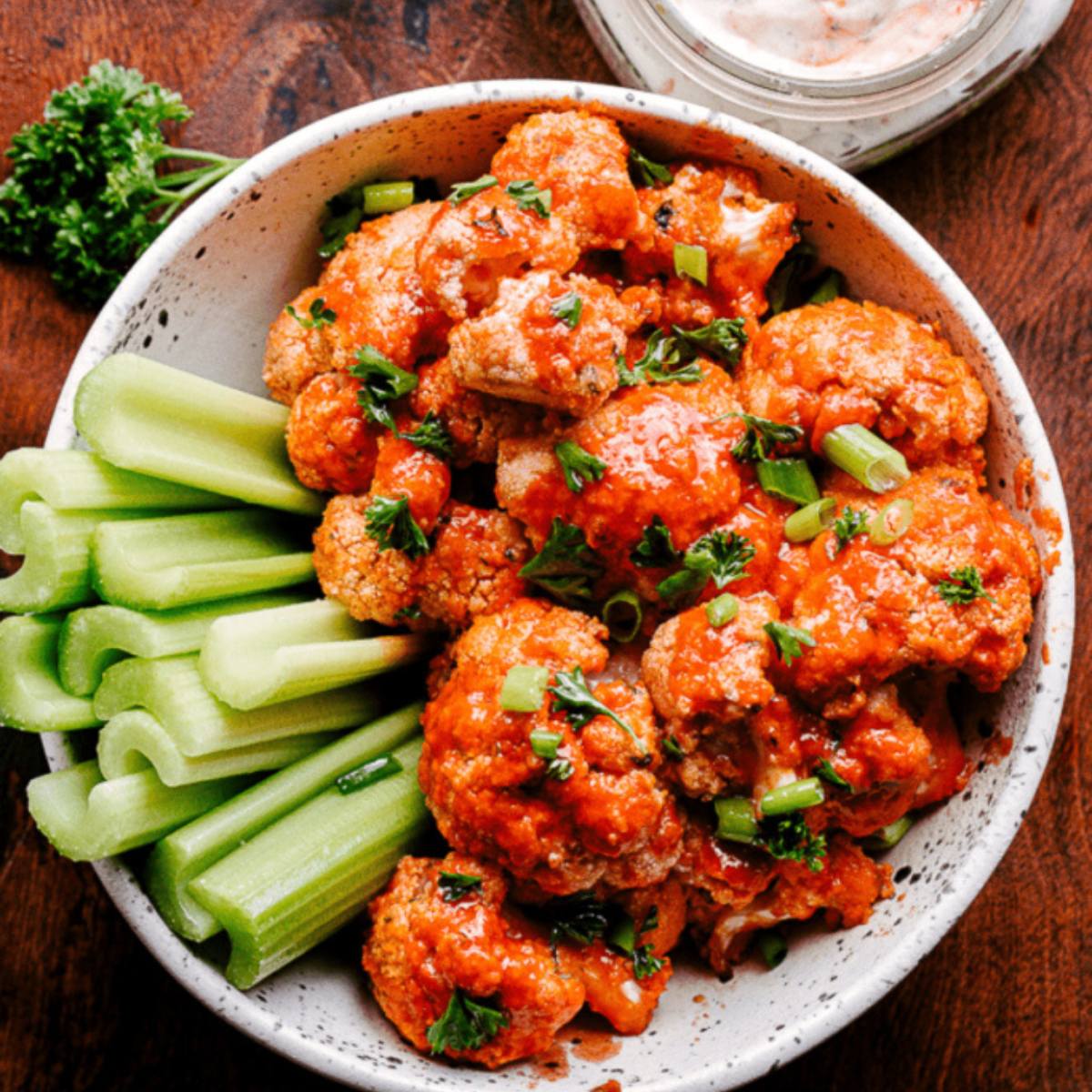 A bowl of Buffalo Cauliflower with celery sticks and a side of ranch dressing.