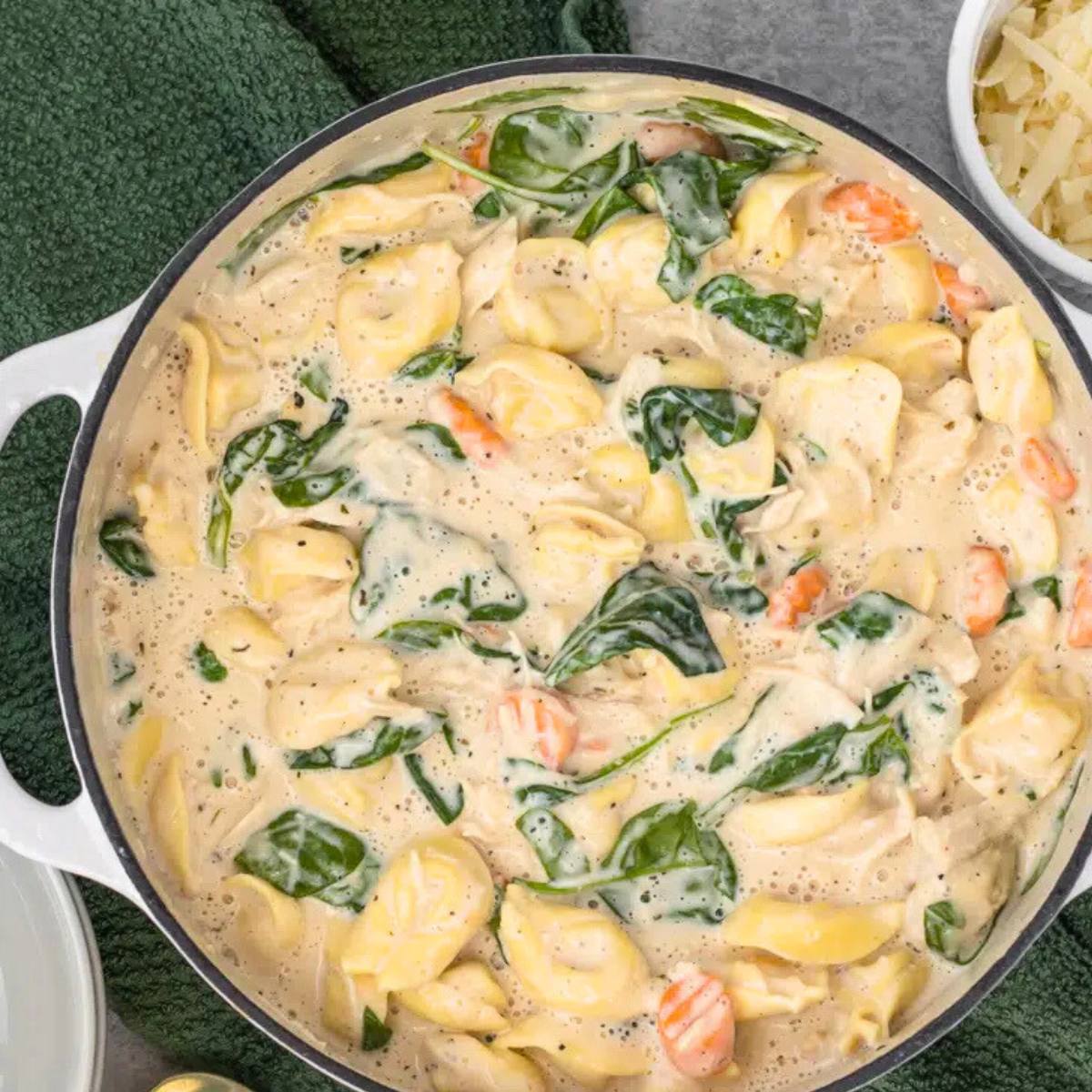 A white pot filled with a creamy tortellini soup. The soup is made with cheese tortellini, spinach, carrots, and a rich, creamy sauce.