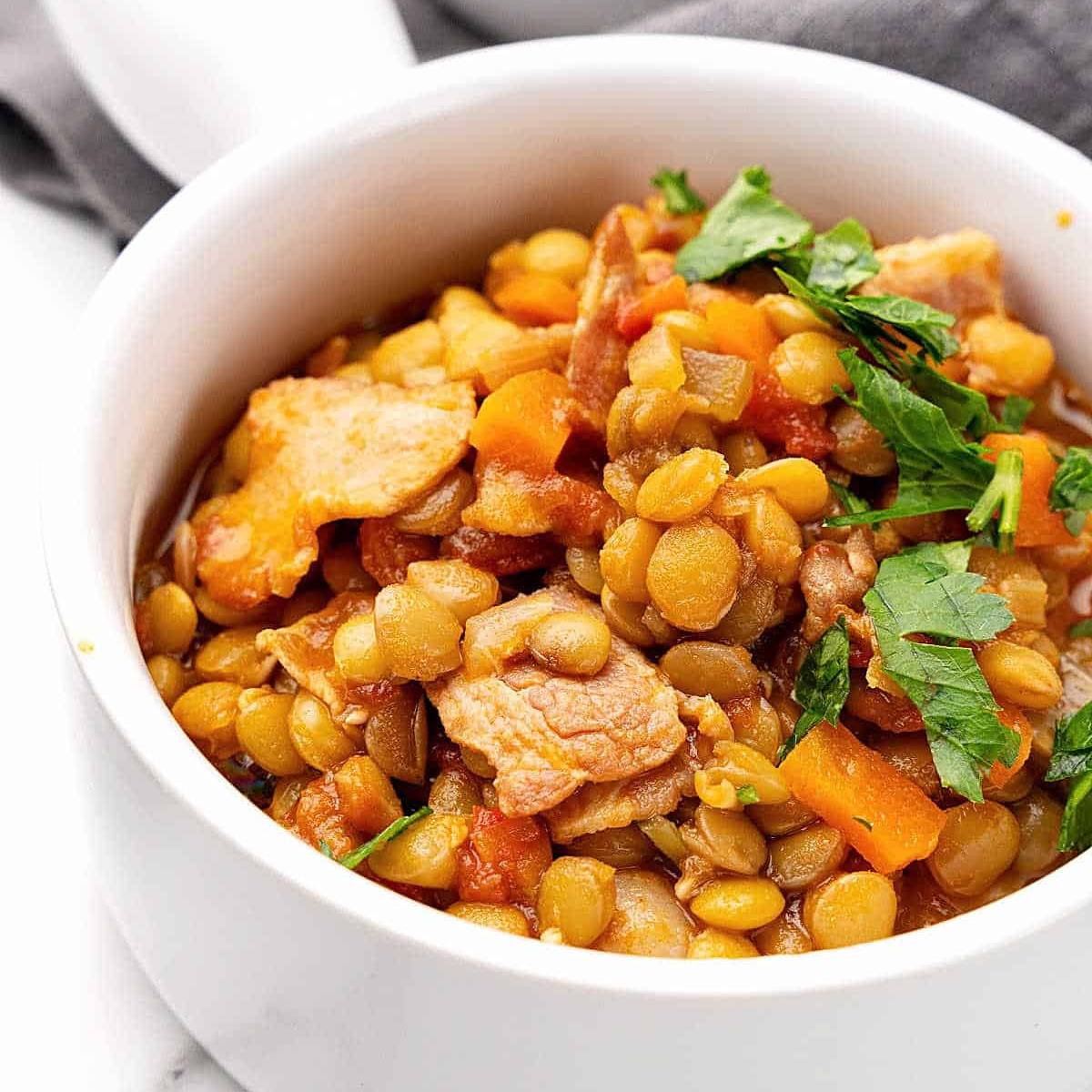 A bowl of hearty lentil soup with chunks of bacon and vegetables, garnished with fresh parsley.