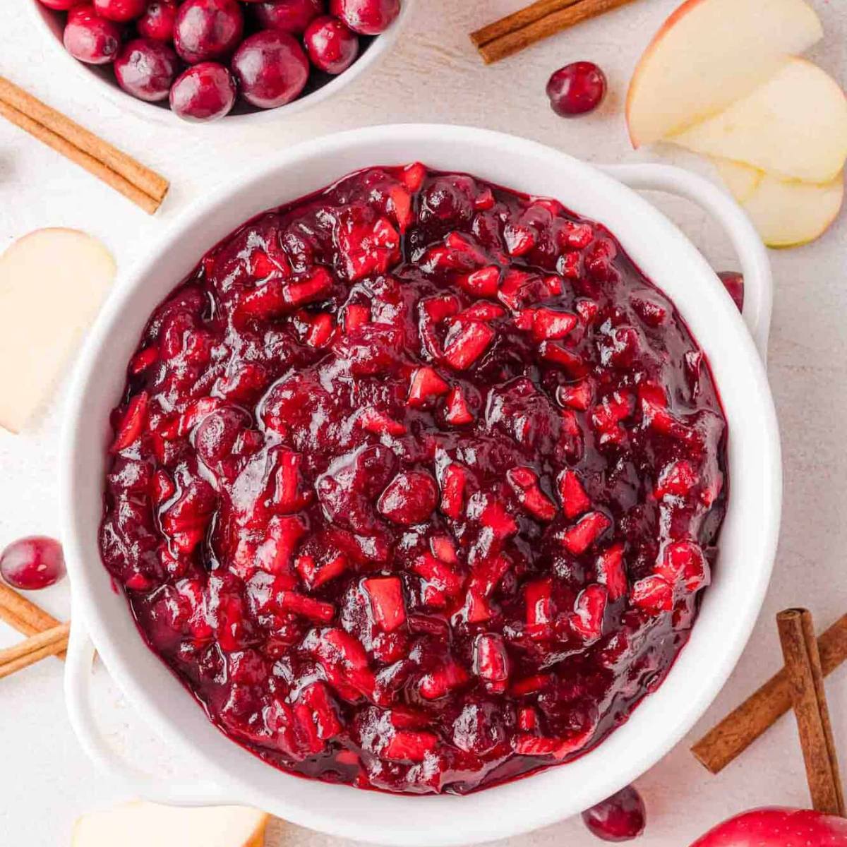 A bowl of homemade cranberry sauce with apples and cinnamon sticks.