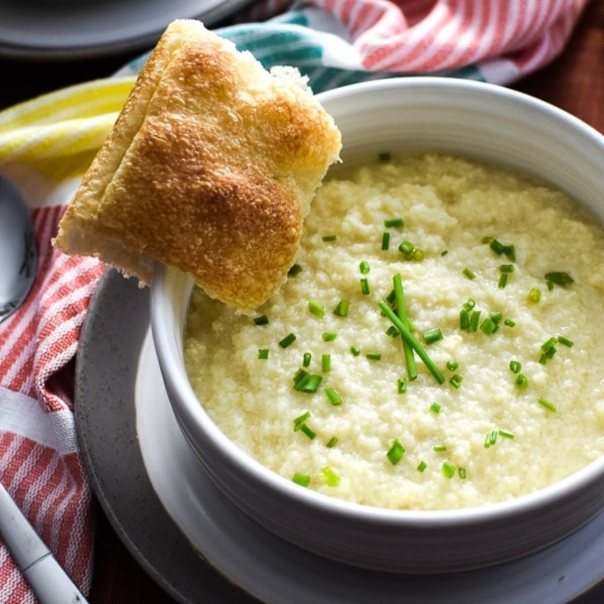 A close-up shot of a white bowl filled with a smooth and creamy cauliflower soup.