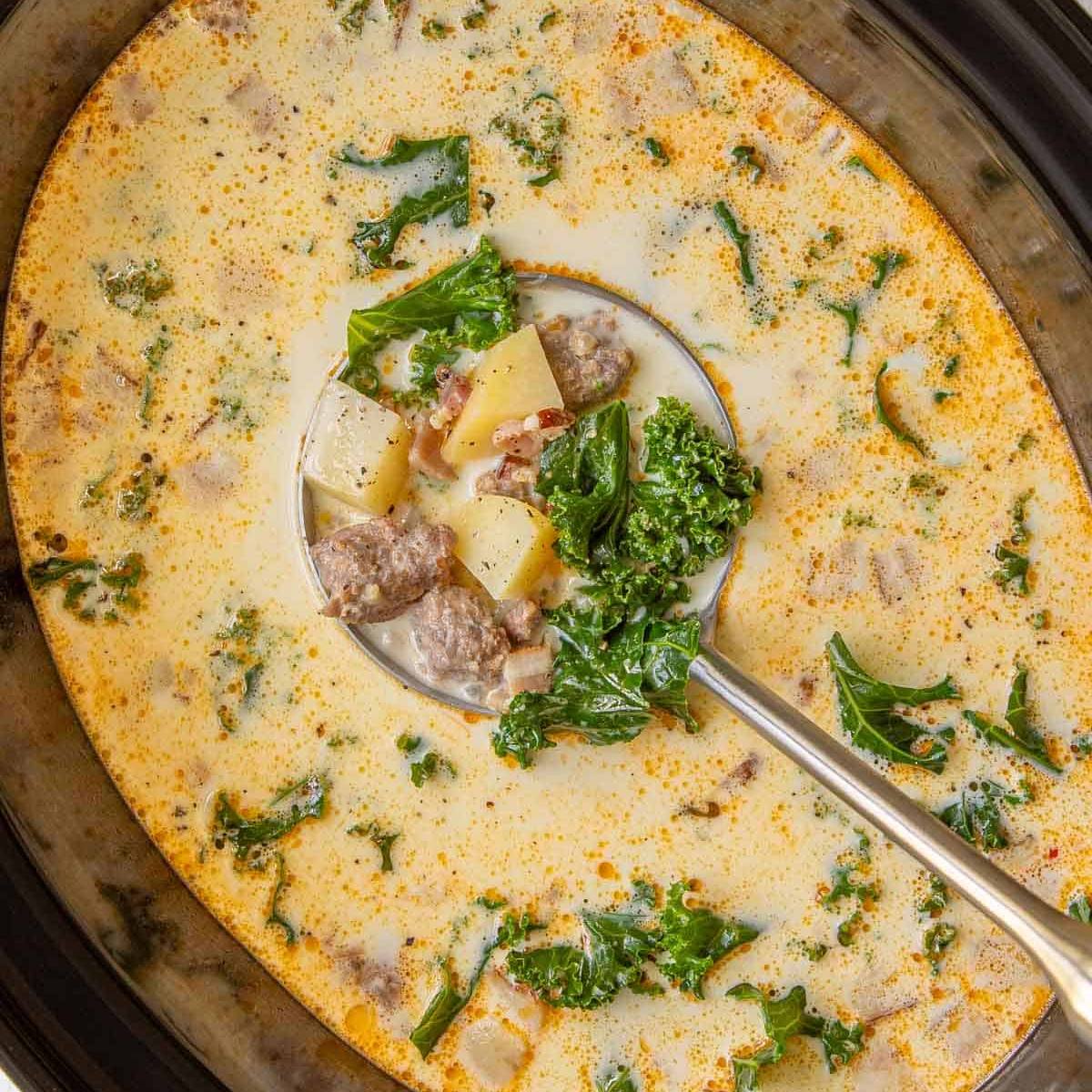 A slow cooker filled with a creamy sausage and potato soup with kale. 